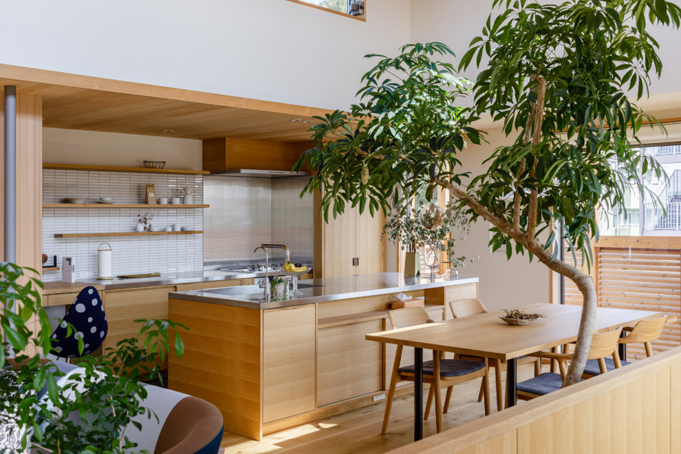 Inredning av ett asiatiskt grå grått kök, med en integrerad diskho, släta luckor, skåp i mellenmörkt trä, bänkskiva i rostfritt stål, vitt stänkskydd, stänkskydd i mosaik, mellanmörkt trägolv, en köksö och brunt golv