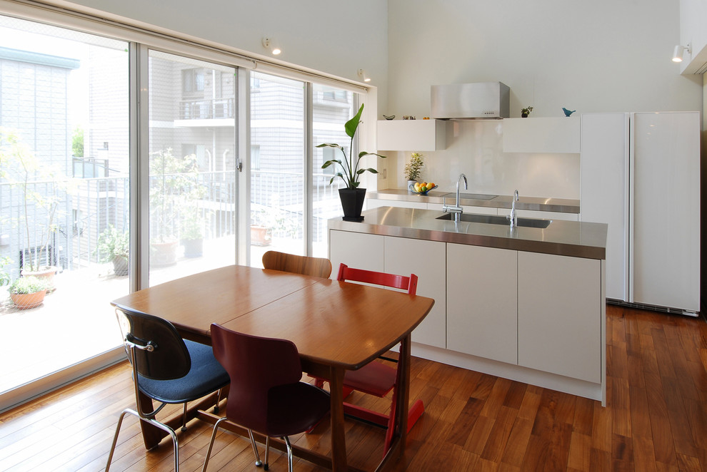 Esempio di una cucina minimalista con lavello integrato, ante lisce, ante bianche, top in acciaio inossidabile, pavimento in legno massello medio e pavimento marrone