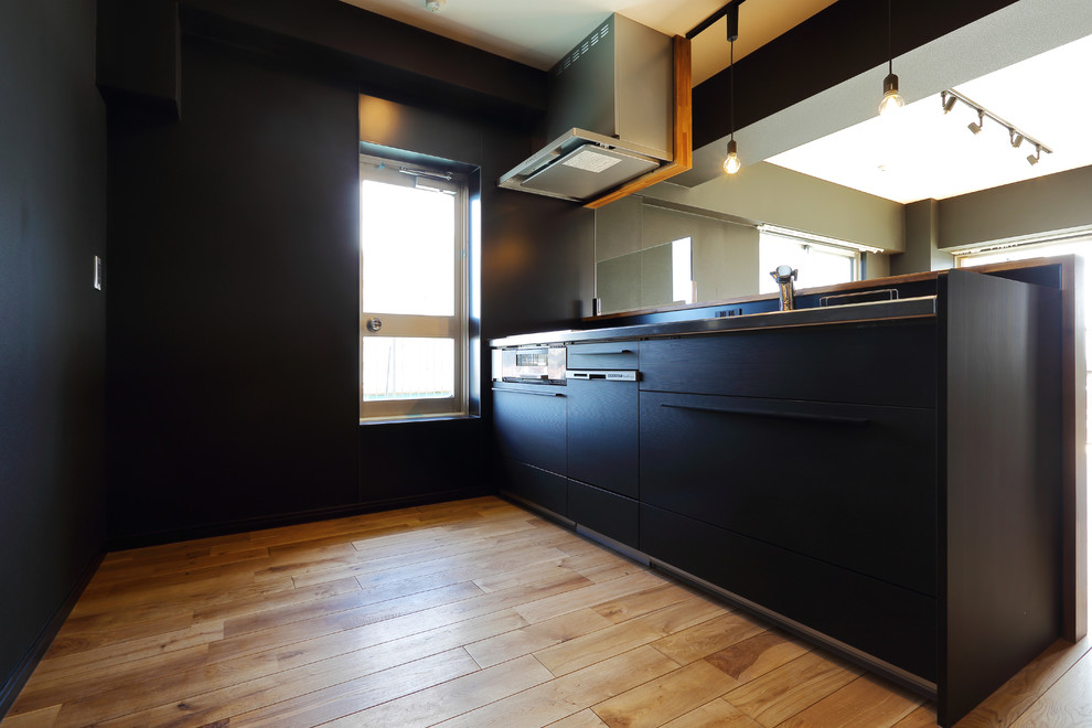 Idées déco pour une cuisine ouverte linéaire moderne de taille moyenne avec des portes de placard noires, un plan de travail en inox, une crédence noire, une crédence en céramique, un sol en bois brun et un sol marron.