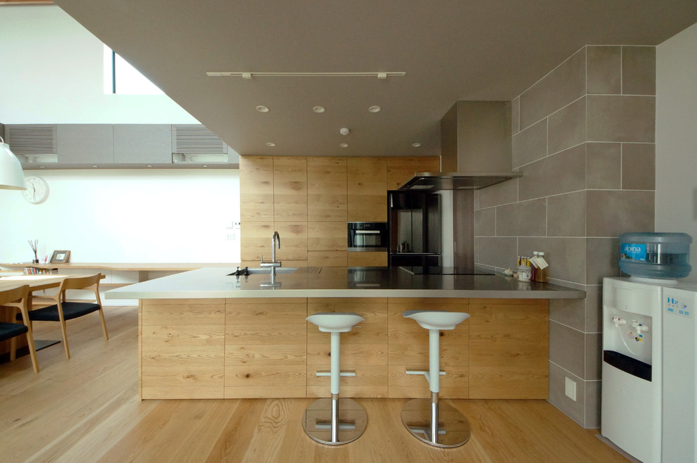 Inredning av ett modernt kök, med en enkel diskho, släta luckor, skåp i mellenmörkt trä, bänkskiva i rostfritt stål, mellanmörkt trägolv, en köksö och brunt golv