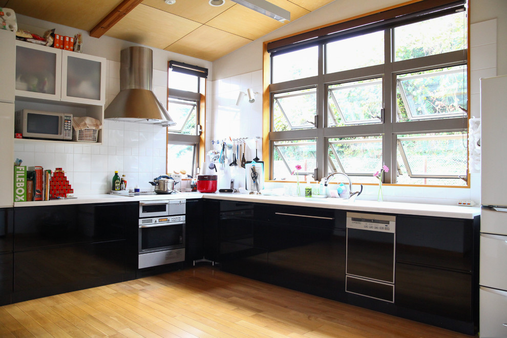 Ejemplo de cocinas en L minimalista grande abierta con puertas de armario negras, salpicadero blanco y encimeras blancas