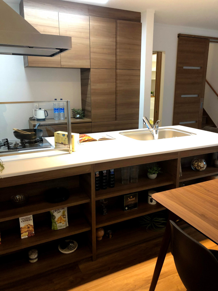 This is an example of a small modern galley open plan kitchen in Other with a submerged sink, flat-panel cabinets, brown cabinets, composite countertops, white splashback, black appliances, plywood flooring, an island, brown floors and white worktops.