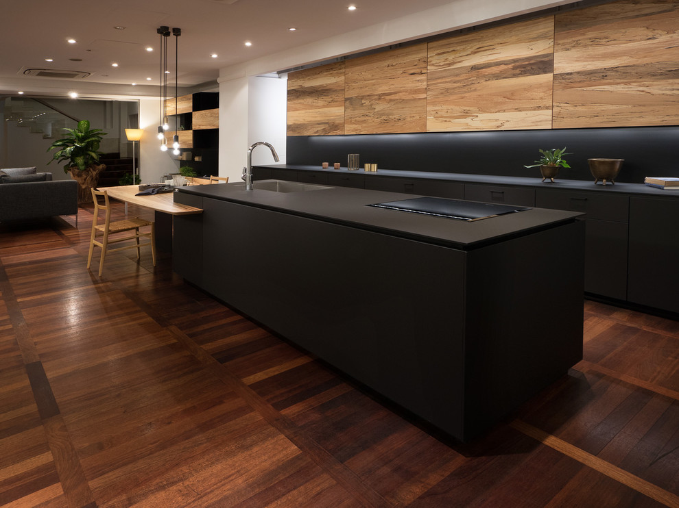Idéer för funkis linjära kök med öppen planlösning, med en undermonterad diskho, luckor med profilerade fronter, svarta skåp, svart stänkskydd, en köksö och brunt golv