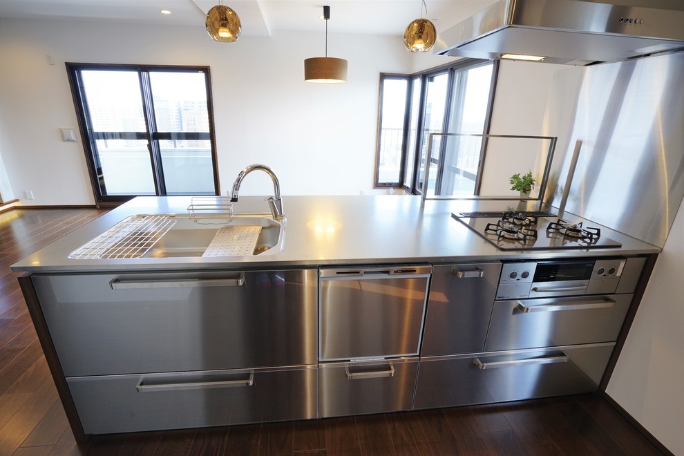 Foto på ett mycket stort funkis linjärt kök med öppen planlösning, med en integrerad diskho, skåp i ljust trä, bänkskiva i rostfritt stål, plywoodgolv, en halv köksö och brunt golv