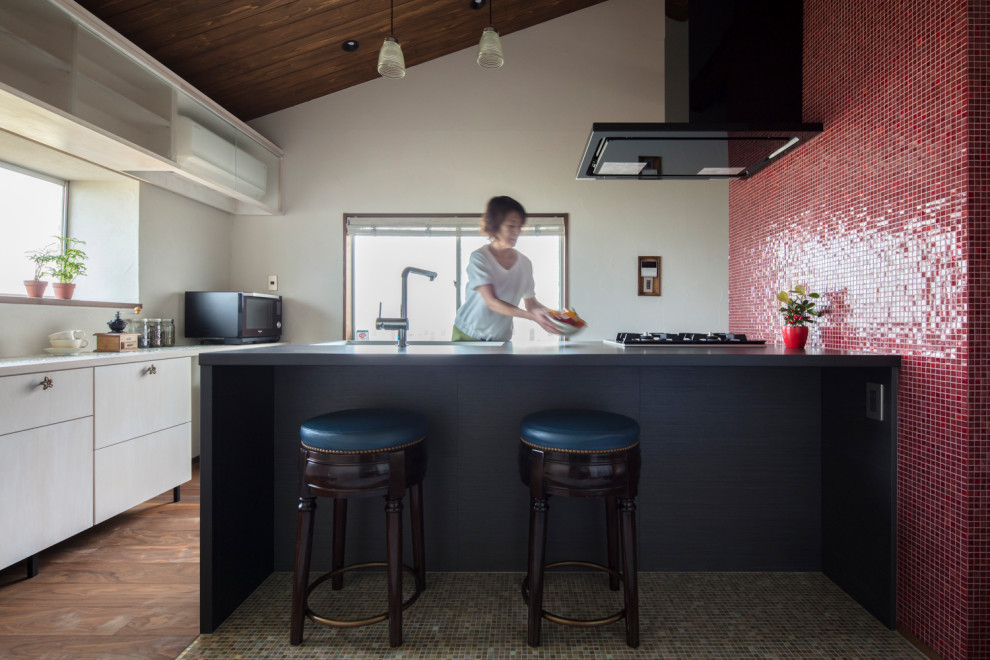 Aménagement d'une cuisine linéaire classique fermée avec un placard à porte vitrée, des portes de placard noires, une crédence rouge, parquet foncé, îlot et plan de travail noir.