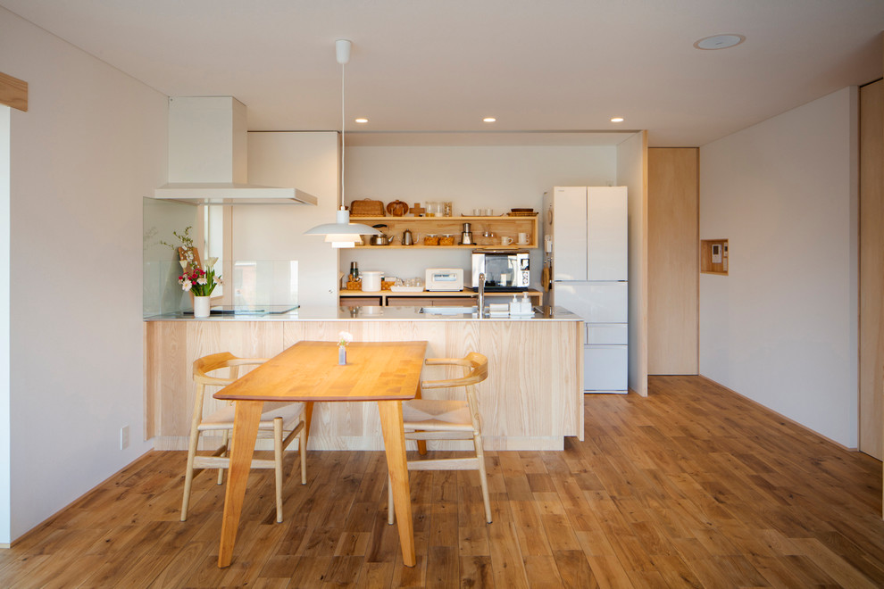 Cette image montre une cuisine ouverte linéaire minimaliste avec un évier intégré, un placard sans porte, un plan de travail en inox, un sol en bois brun, une péninsule et un sol marron.