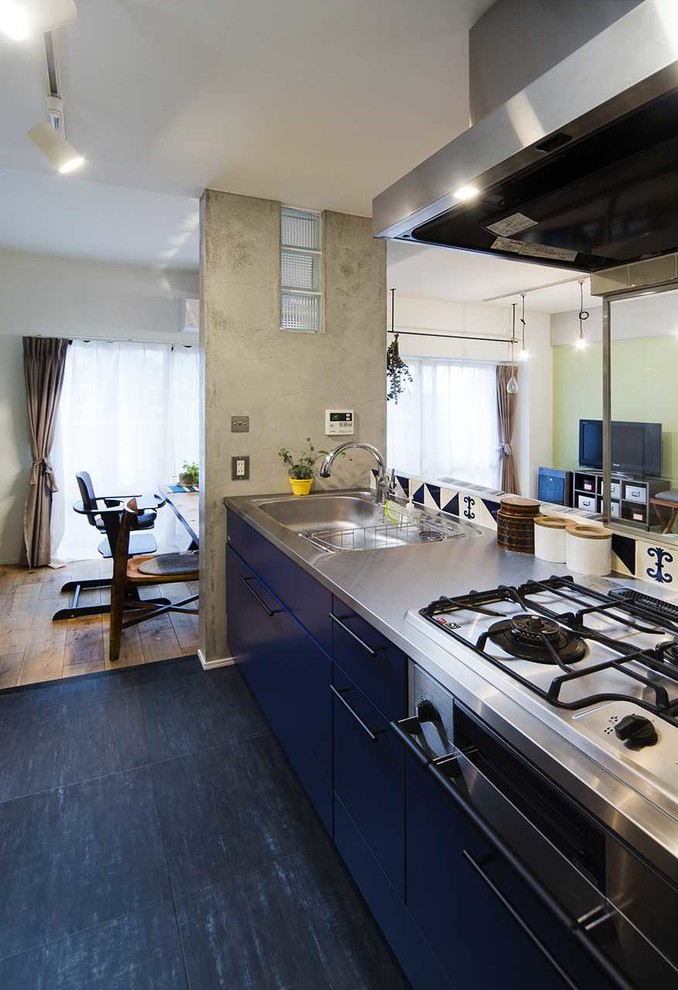 Foto di una cucina industriale con lavello integrato, ante lisce, ante blu, top in acciaio inossidabile, penisola e pavimento nero