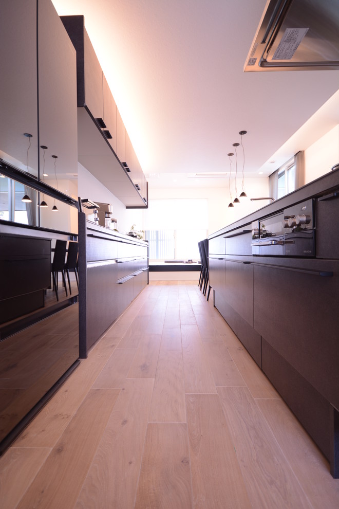 Idée de décoration pour une cuisine minimaliste avec un placard à porte plane, des portes de placard noires, une crédence noire, un électroménager noir, parquet clair et un sol blanc.