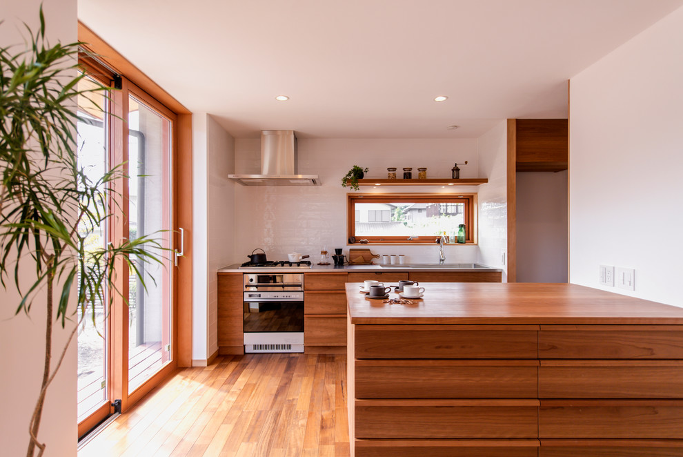Foto på ett orientaliskt kök, med en enkel diskho, luckor med infälld panel, skåp i mellenmörkt trä, träbänkskiva, vitt stänkskydd, mellanmörkt trägolv, en halv köksö och brunt golv