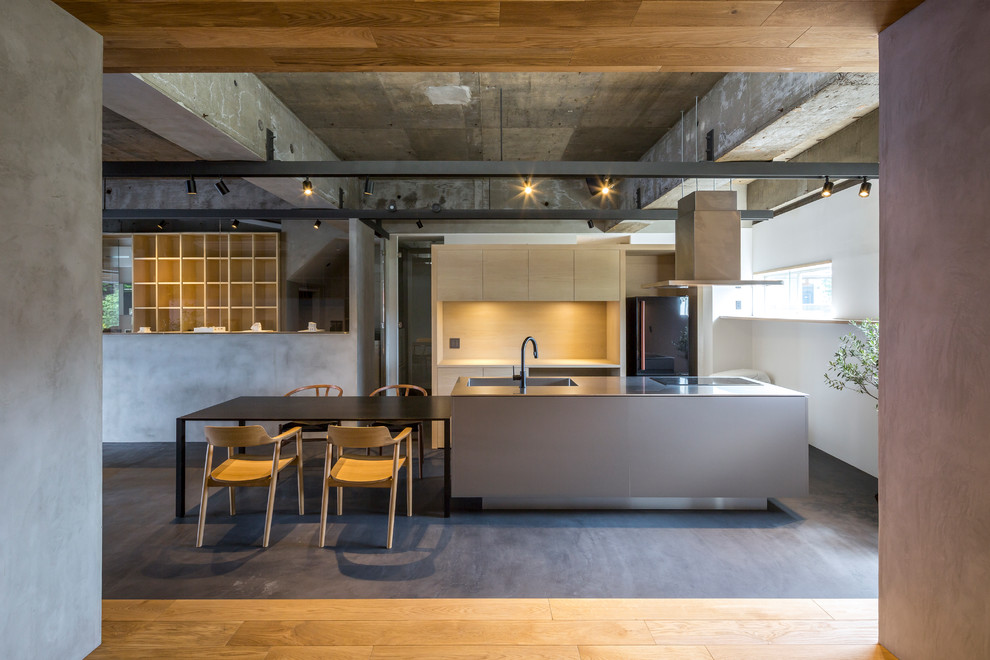 Cette photo montre une cuisine ouverte industrielle en inox de taille moyenne avec un évier intégré, un placard à porte affleurante, un plan de travail en inox, un électroménager noir, sol en béton ciré, îlot, un sol gris et un plan de travail gris.