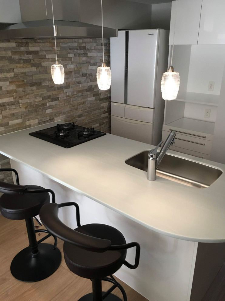 Example of a mid-sized minimalist single-wall light wood floor and beige floor open concept kitchen design in Fukuoka with an undermount sink, white cabinets, solid surface countertops, white backsplash, shiplap backsplash, black appliances, a peninsula and green countertops
