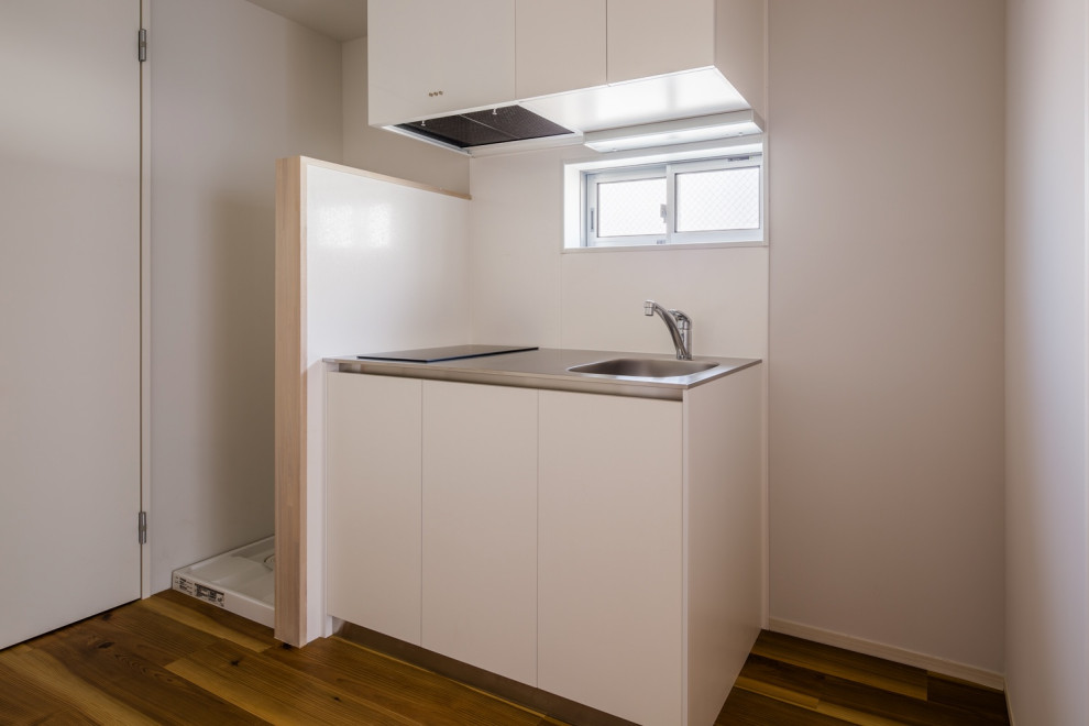 東京23区にある低価格の小さな北欧スタイルのおしゃれなキッチン (アンダーカウンターシンク、インセット扉のキャビネット、白いキャビネット、ステンレスカウンター、白いキッチンパネル、モザイクタイルのキッチンパネル、白い調理設備、無垢フローリング、茶色い床、グレーのキッチンカウンター、塗装板張りの天井) の写真