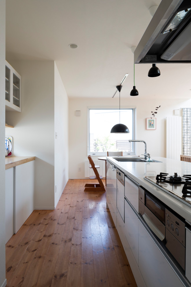 他の地域にある北欧スタイルのおしゃれなキッチン (シングルシンク、フラットパネル扉のキャビネット、白いキャビネット、無垢フローリング、茶色い床) の写真