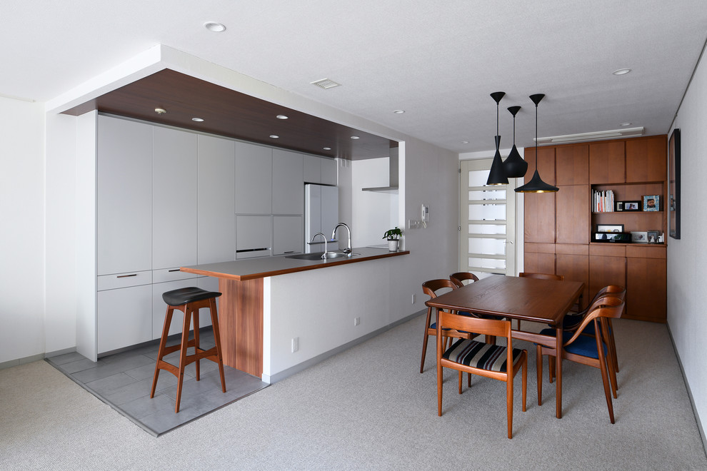 Aménagement d'une cuisine ouverte linéaire scandinave en bois brun avec un évier encastré, un placard à porte affleurante, un électroménager en acier inoxydable, moquette, une péninsule et un sol gris.