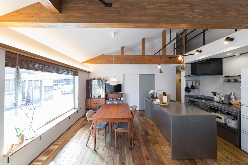 Industriell inredning av ett grå grått kök, med öppna hyllor, grå skåp, bänkskiva i rostfritt stål, rostfria vitvaror, mellanmörkt trägolv, en köksö och brunt golv