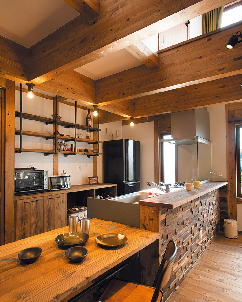 Photo of a world-inspired single-wall kitchen in Other with a single-bowl sink, flat-panel cabinets, medium wood cabinets, light hardwood flooring, a breakfast bar, brown floors and brown worktops.