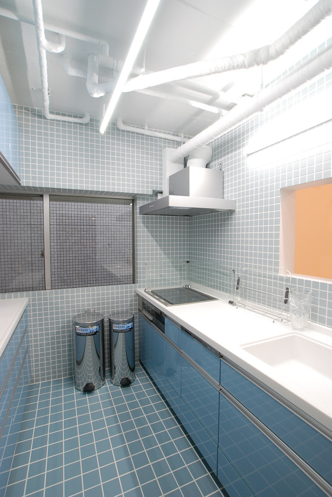 Immagine di una cucina parallela industriale chiusa con lavello integrato, ante lisce, ante blu, paraspruzzi con lastra di vetro e pavimento in gres porcellanato