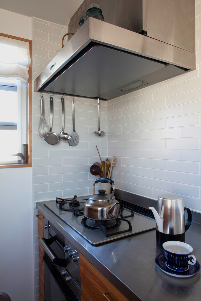 This is an example of a medium sized scandinavian galley enclosed kitchen in Tokyo with an integrated sink, shaker cabinets, medium wood cabinets, stainless steel worktops, white splashback, ceramic splashback, stainless steel appliances, carpet and multi-coloured floors.
