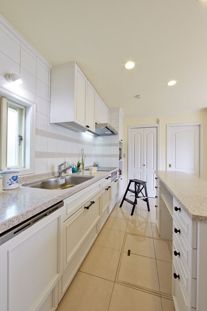 Inredning av ett klassiskt linjärt kök, med en enkel diskho, luckor med infälld panel, vita skåp, vitt stänkskydd, en köksö och beiget golv