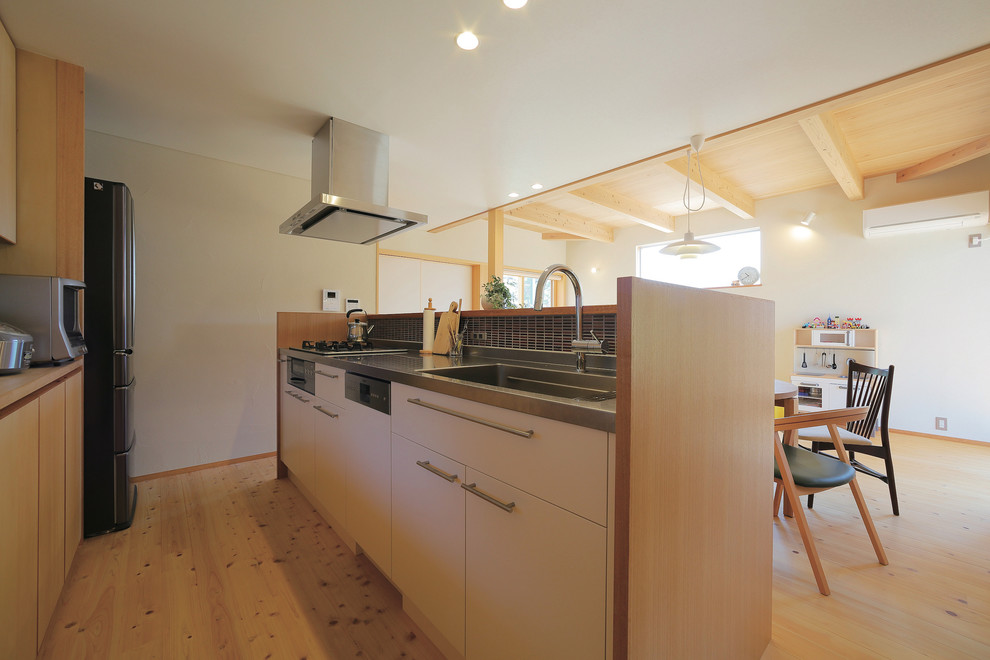 Foto på ett skandinaviskt kök, med en integrerad diskho, släta luckor, skåp i ljust trä, bänkskiva i rostfritt stål, brunt stänkskydd, stänkskydd i mosaik, rostfria vitvaror, ljust trägolv och en köksö