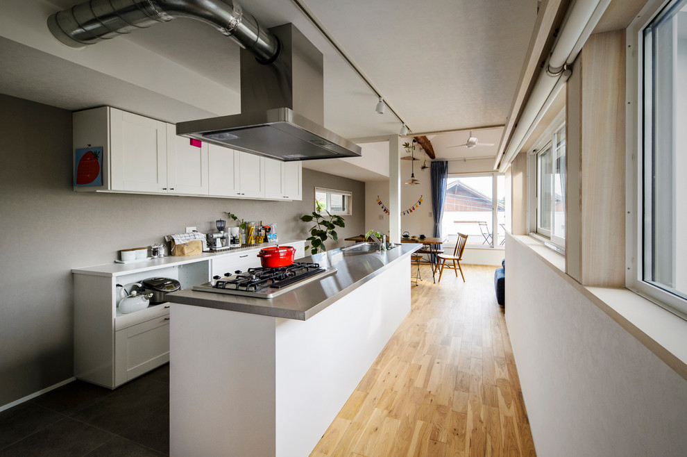 北欧スタイルのおしゃれなキッチン (シングルシンク、落し込みパネル扉のキャビネット、白いキャビネット、ステンレスカウンター、淡色無垢フローリング、茶色い床) の写真