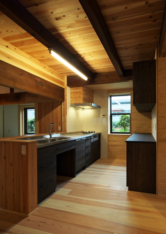 Aménagement d'une cuisine linéaire asiatique avec un évier 1 bac, un placard à porte plane, des portes de placard noires, un sol en bois brun, une péninsule et un sol marron.