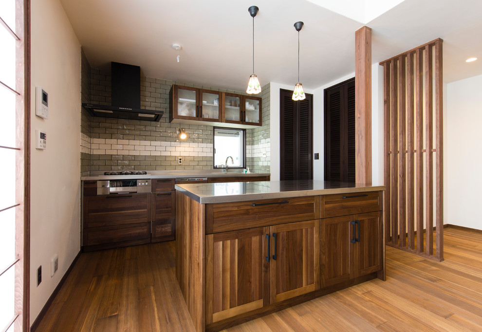 Cette photo montre une cuisine nature en bois vieilli avec un placard avec porte à panneau encastré, un plan de travail en inox, un sol en bois brun, îlot et un sol marron.