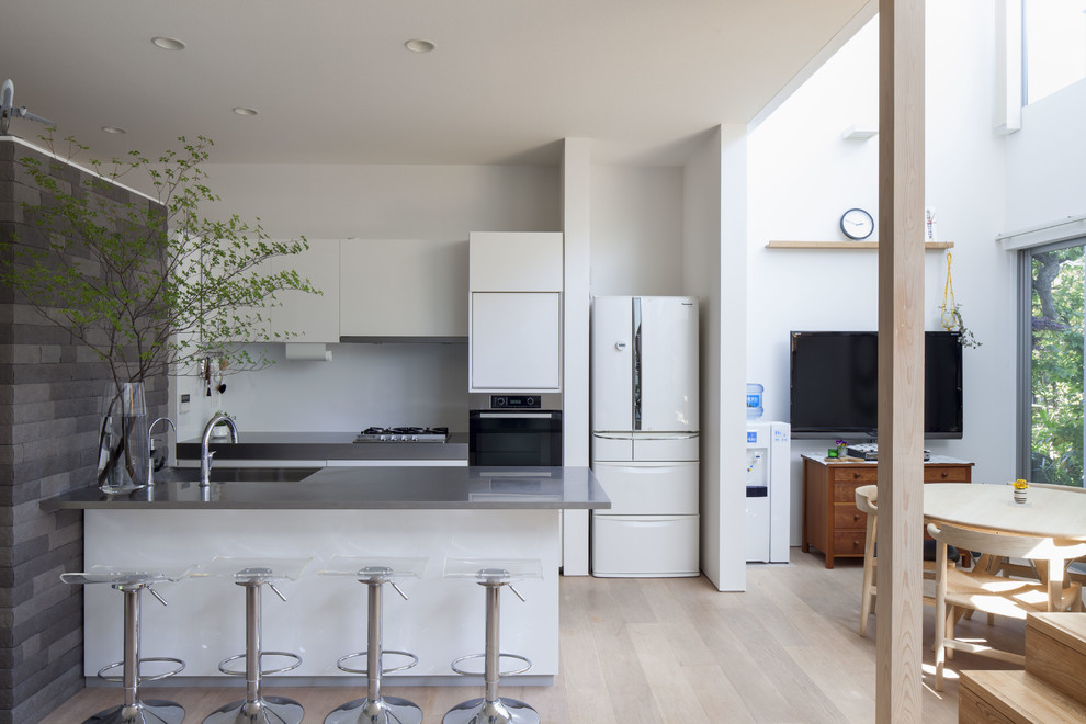 Идея дизайна: параллельная кухня-гостиная в современном стиле с одинарной мойкой, плоскими фасадами, белыми фасадами, столешницей из нержавеющей стали, белым фартуком, деревянным полом, полуостровом и коричневым полом