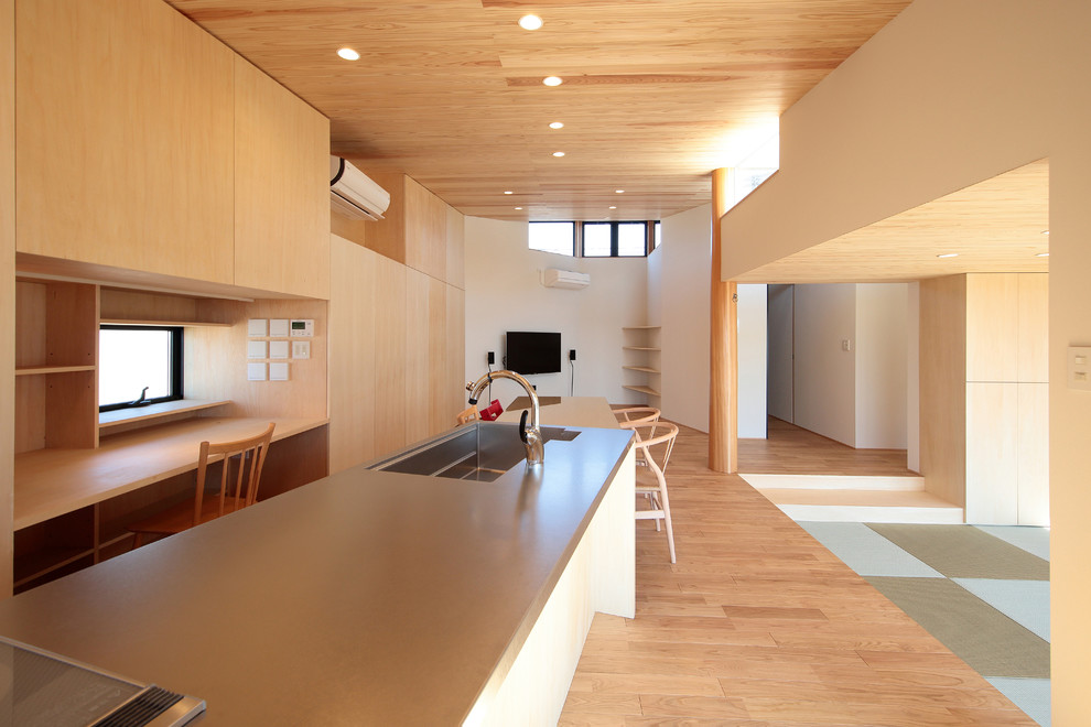 Cette image montre une cuisine ouverte linéaire asiatique avec un évier 1 bac, un placard sans porte, un plan de travail en inox, parquet clair, îlot et un sol marron.