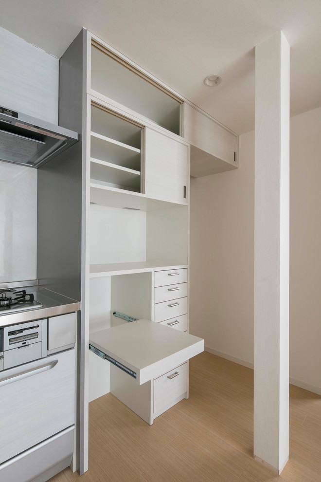 Foto på ett litet minimalistiskt kök, med en undermonterad diskho, luckor med profilerade fronter, vita skåp, bänkskiva i rostfritt stål, vitt stänkskydd, stänkskydd i trä, svarta vitvaror, ljust trägolv, en köksö och beiget golv