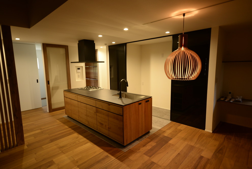 Idéer för ett modernt svart kök, med en undermonterad diskho, släta luckor, skåp i mellenmörkt trä, brunt stänkskydd, stänkskydd i trä, svarta vitvaror, mellanmörkt trägolv och brunt golv