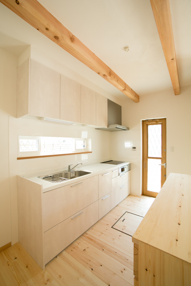 Réalisation d'une cuisine linéaire nordique en bois clair avec un évier encastré, un placard à porte plane, une crédence blanche, parquet clair, un sol beige et un plan de travail blanc.