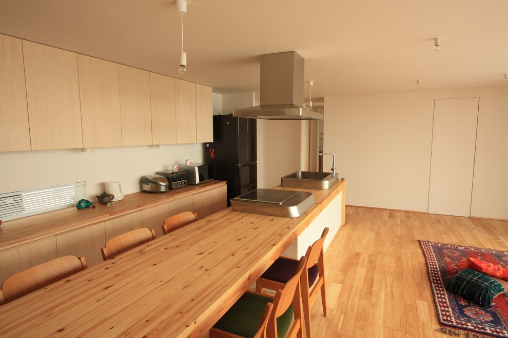 На фото: узкая параллельная кухня-гостиная в восточном стиле с открытыми фасадами, светлыми деревянными фасадами, деревянной столешницей, техникой из нержавеющей стали и островом