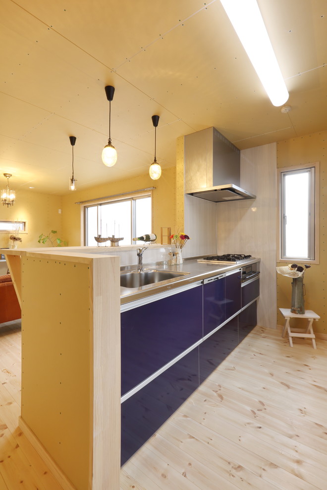 他の地域にあるエクレクティックスタイルのおしゃれなキッチン (シングルシンク、青いキャビネット、ステンレスカウンター、淡色無垢フローリング、フラットパネル扉のキャビネット、白いキッチンパネル、茶色い床) の写真
