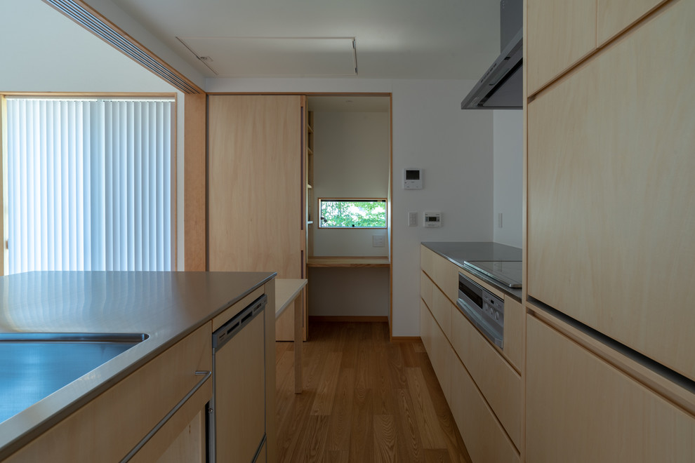 Zweizeilige Moderne Wohnküche mit integriertem Waschbecken, flächenbündigen Schrankfronten, hellen Holzschränken, Edelstahl-Arbeitsplatte, Sperrholzboden und Kücheninsel in Sonstige