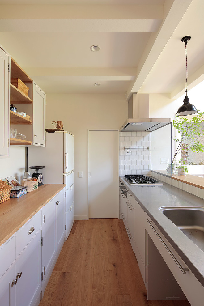 Idéer för att renovera ett minimalistiskt linjärt kök med öppen planlösning, med en integrerad diskho, luckor med infälld panel, vita skåp, träbänkskiva, vitt stänkskydd, vita vitvaror, mellanmörkt trägolv, en halv köksö och brunt golv