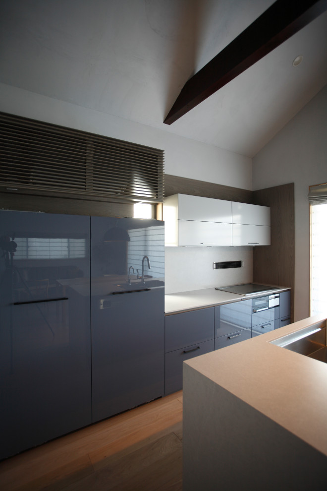 Inredning av ett minimalistiskt grå grått kök, med en undermonterad diskho, släta luckor, grå skåp, bänkskiva i kvarts, grått stänkskydd, rostfria vitvaror, ljust trägolv, en köksö och beiget golv