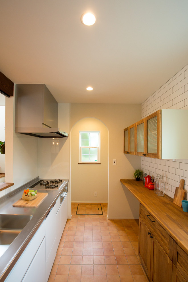 Exempel på ett asiatiskt brun linjärt brunt kök, med en enkel diskho, släta luckor, vita skåp, bänkskiva i rostfritt stål, vitt stänkskydd, klinkergolv i terrakotta, en halv köksö och orange golv