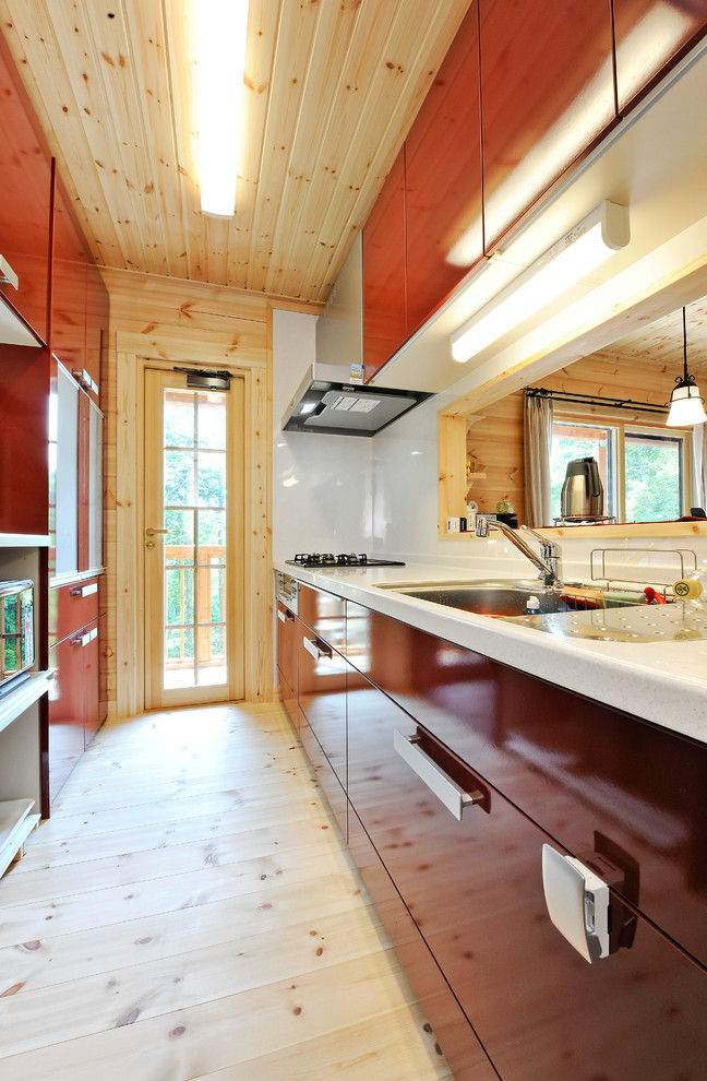 Idéer för att renovera ett avskilt, mellanstort nordiskt linjärt kök, med en enkel diskho, röda skåp, bänkskiva i koppar, rött stänkskydd, glaspanel som stänkskydd, rostfria vitvaror och ljust trägolv