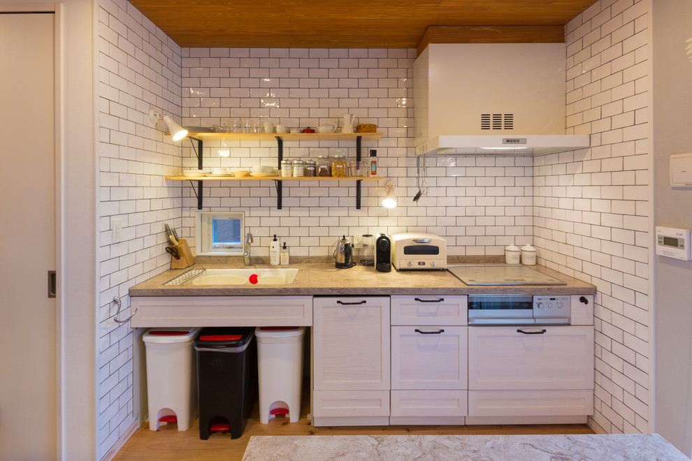 Example of a large danish galley medium tone wood floor and brown floor open concept kitchen design in Other with an undermount sink, recessed-panel cabinets, white cabinets, solid surface countertops, white backsplash, subway tile backsplash, white appliances, an island and gray countertops