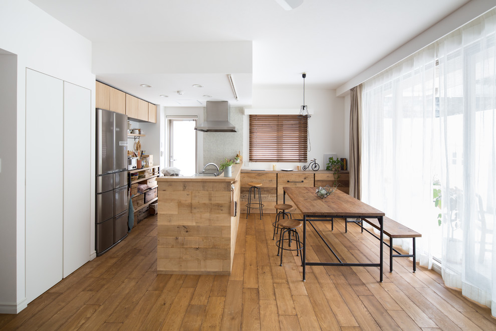 Inspiration pour une cuisine américaine parallèle asiatique en bois clair avec un placard à porte plane, un électroménager en acier inoxydable, un sol en bois brun et un sol marron.