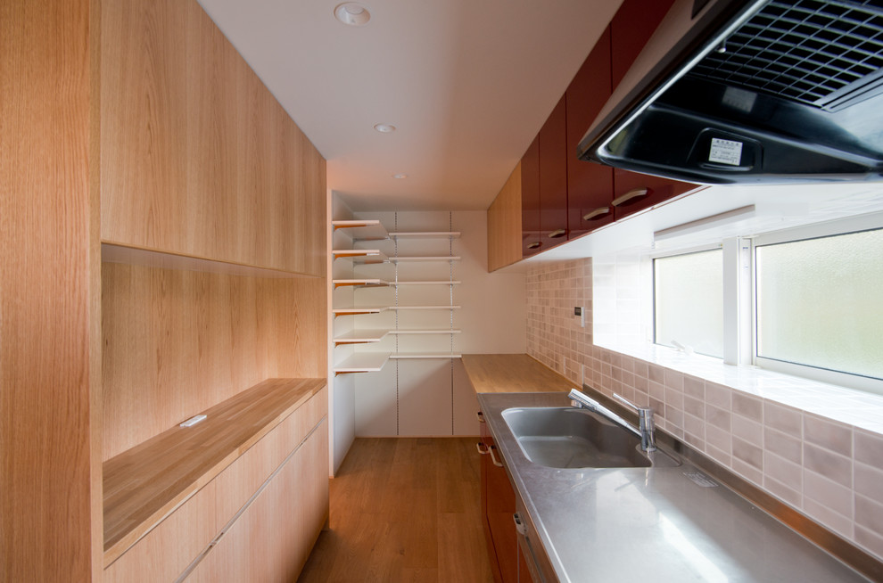 Mid-sized minimalist single-wall light wood floor and beige floor kitchen photo in Other with flat-panel cabinets, red cabinets, stainless steel countertops, porcelain backsplash and stainless steel appliances