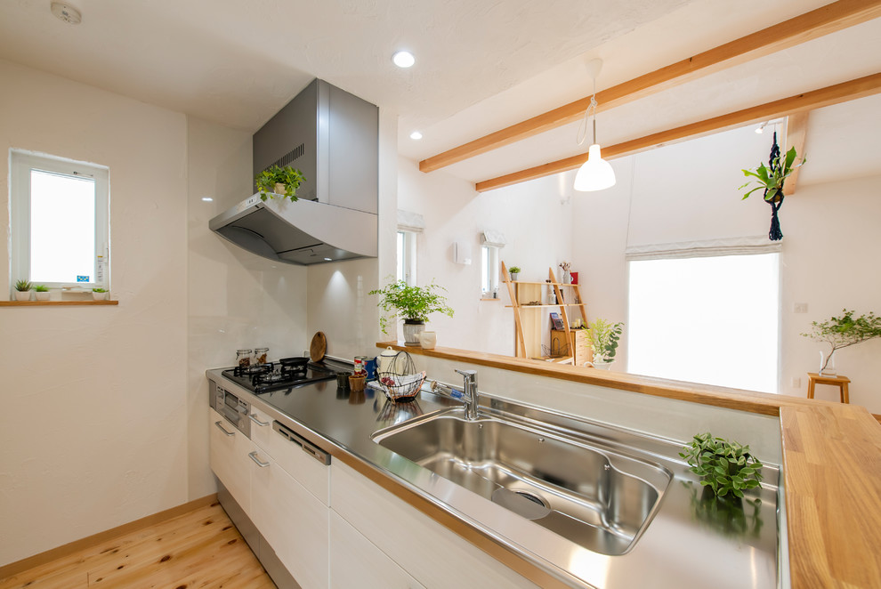 Immagine di una cucina minimalista di medie dimensioni con ante bianche, paraspruzzi bianco, pavimento in legno massello medio e pavimento beige