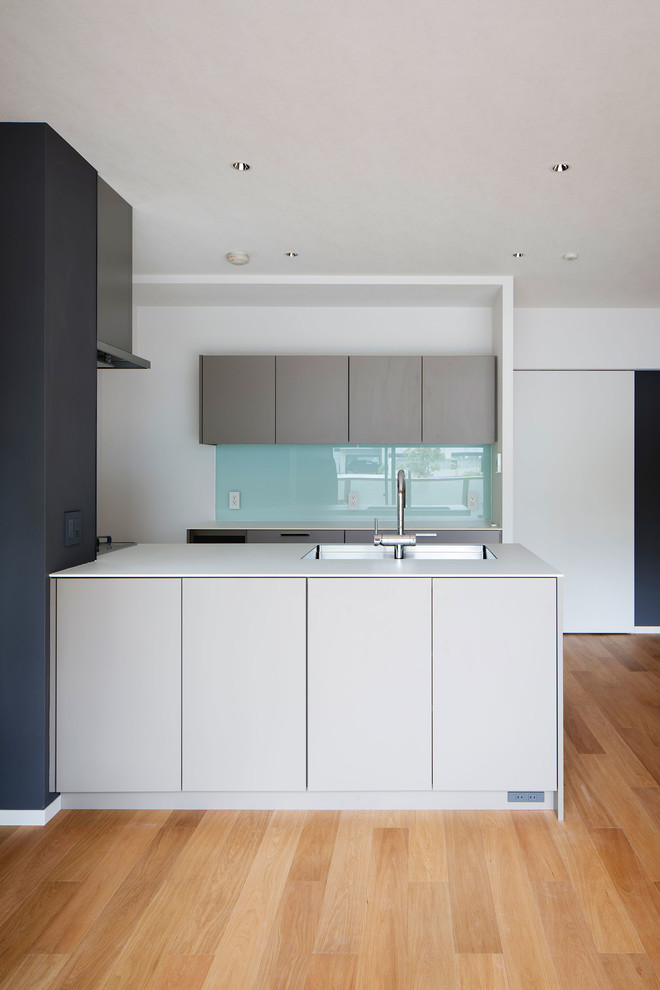 Design ideas for a small contemporary galley open plan kitchen in Osaka with a built-in sink, beaded cabinets, grey cabinets, laminate countertops, white splashback, glass tiled splashback, plywood flooring, an island, beige floors and white worktops.