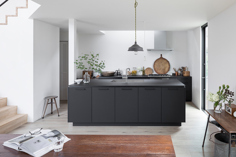 Foto på ett rustikt svart linjärt kök med öppen planlösning, med en undermonterad diskho, luckor med profilerade fronter, svarta skåp, rostfria vitvaror, ljust trägolv, en köksö och beiget golv