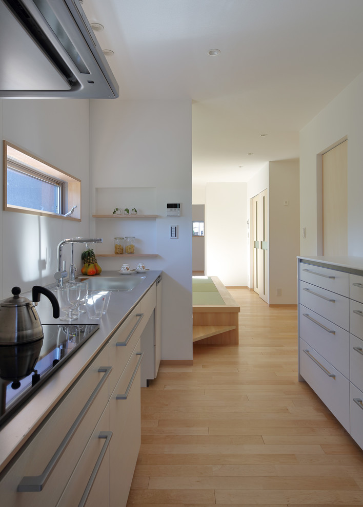 Bild på ett avskilt funkis linjärt kök, med vita skåp, bänkskiva i rostfritt stål, vitt stänkskydd och ljust trägolv