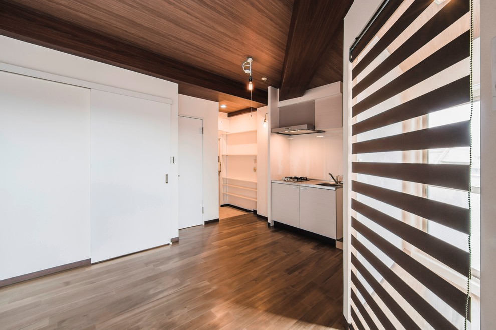 Inredning av ett modernt linjärt kök med öppen planlösning, med luckor med profilerade fronter, vita skåp, bänkskiva i koppar, vitt stänkskydd, rostfria vitvaror, plywoodgolv och brunt golv