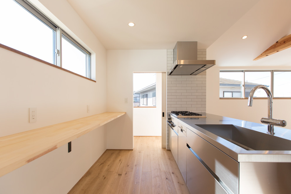 Idéer för ett mellanstort modernt beige linjärt kök med öppen planlösning, med en integrerad diskho, bänkskiva i rostfritt stål, stänkskydd i stickkakel, rostfria vitvaror, mellanmörkt trägolv, en halv köksö och beiget golv