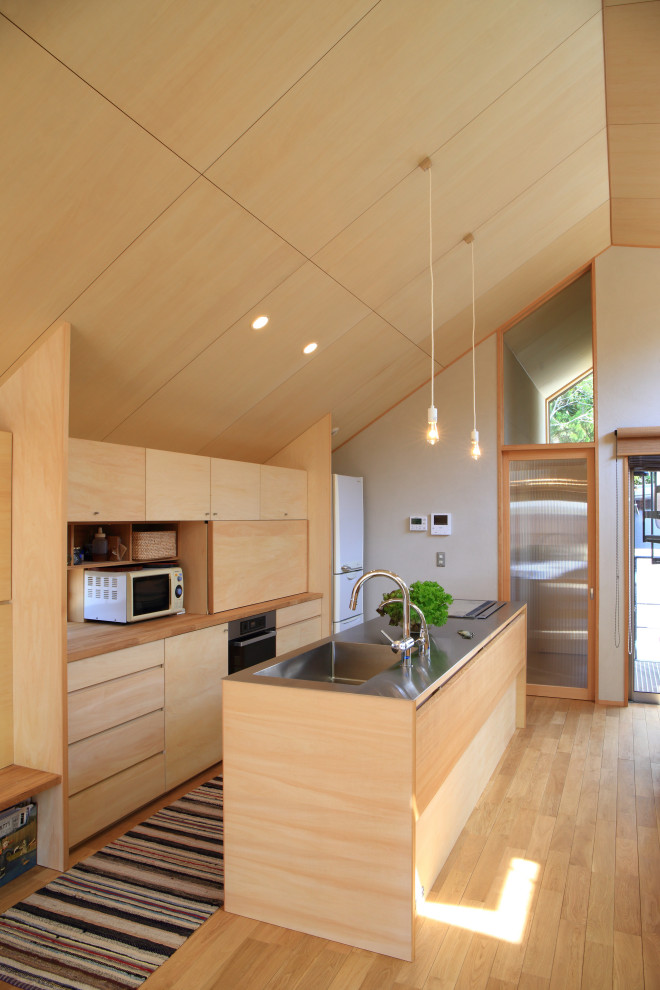 Foto på ett rustikt beige linjärt kök med öppen planlösning, med en integrerad diskho, släta luckor, skåp i ljust trä, bänkskiva i rostfritt stål, vita vitvaror, mellanmörkt trägolv, en köksö och beiget golv