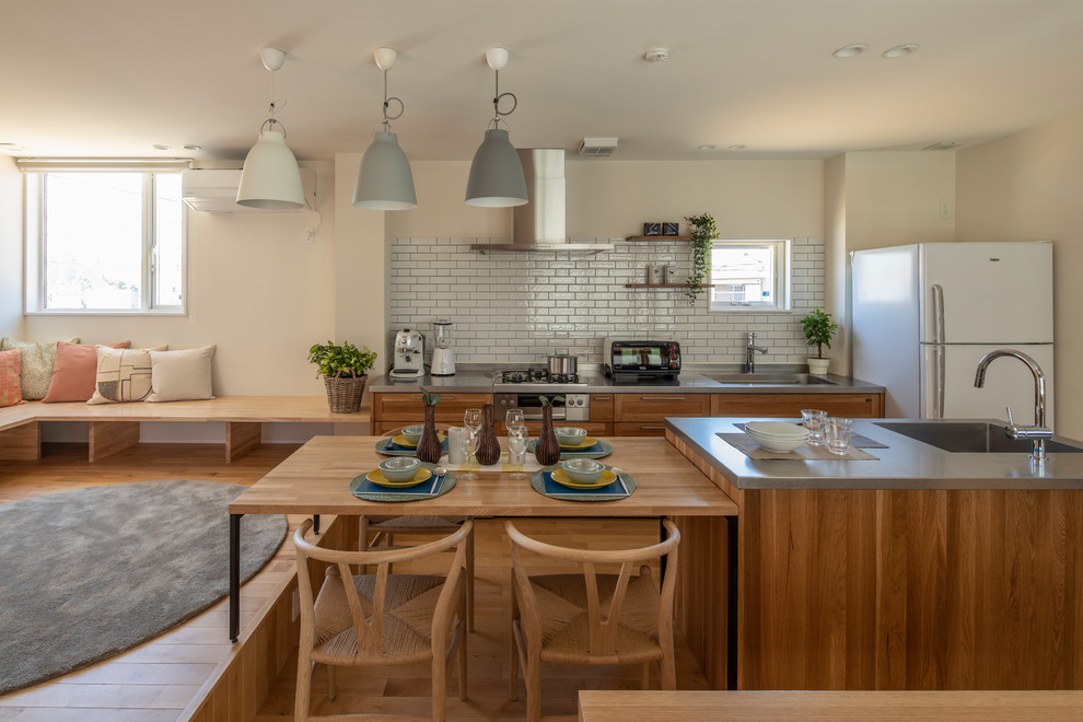 Imagen de cocina comedor asiática con fregadero de un seno, armarios estilo shaker, puertas de armario de madera oscura, encimera de acero inoxidable, salpicadero blanco, salpicadero de azulejos tipo metro, electrodomésticos blancos, suelo de madera en tonos medios, una isla, suelo beige y encimeras grises